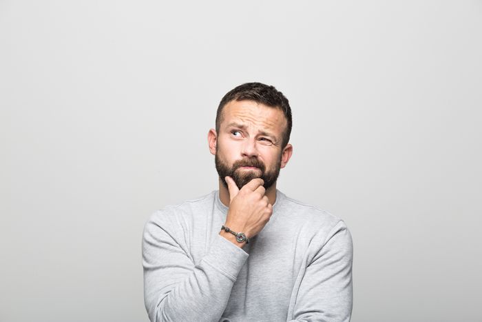 A bearded man in front of a white background looking thoughtful.